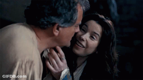 A Man Kissing A Woman On The Cheek In A Dark Room . GIF