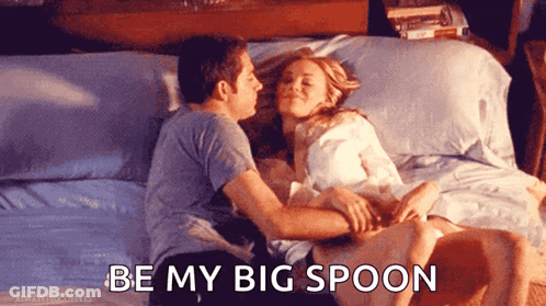 A Man Kissing A Woman On The Forehead While Laying On A Bed With The Words " Be My Big Spoon " Below Them GIF