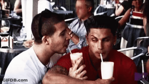 A Man Kissing Another Man On The Cheek While Drinking A Milkshake GIF