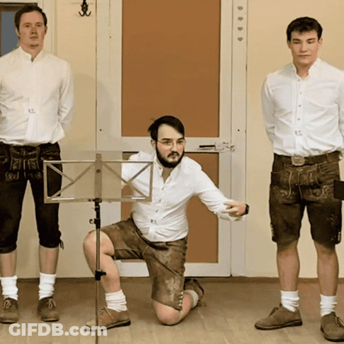 A Man Kneeling Down In Front Of A Music Stand With Two Other Men Standing Behind Him GIF