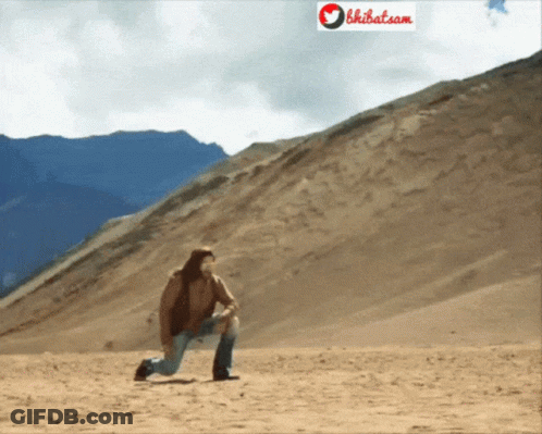 A Man Kneeling Down In The Desert With A Sign That Says Bhibat.com Behind Him GIF