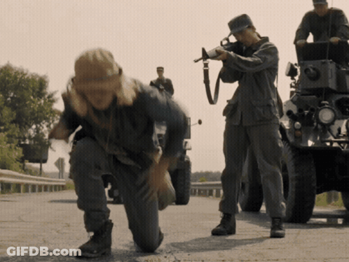 A Man Kneeling Down With A Gun While Another Man Looks On GIF