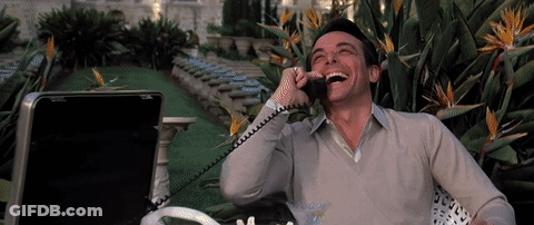 A Man Laughs While Talking On A Phone Outside GIF