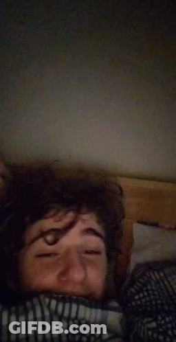 A Man Laying In Bed With His Eyes Closed And A Blanket On His Head . GIF