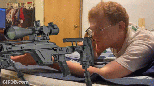 A Man Laying On A Bed Looking At A Rifle GIF