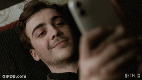 A Man Laying On A Bed Looking At His Phone With Netflix Written On The Bottom Right GIF