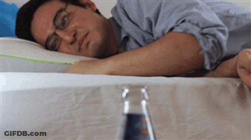 A Man Laying On A Bed With A Bottle Of Water In The Foreground GIF