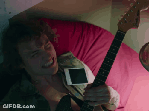 A Man Laying On A Bed With A Guitar And A Cell Phone GIF