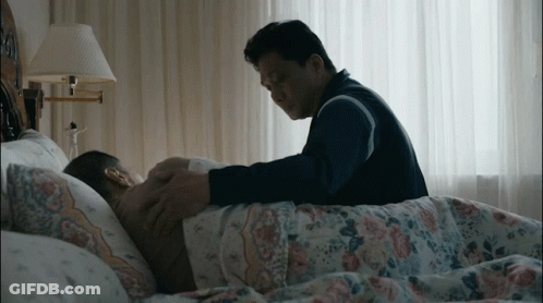 A Man Laying On A Bed With A Lamp Behind Him GIF