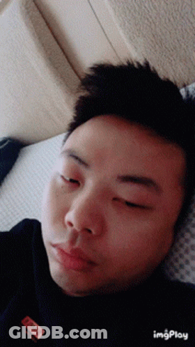 A Man Laying On A Bed With His Eyes Closed And A Label On His Shirt That Says ' I Am A ' GIF