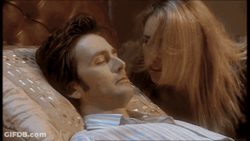 A Man Laying On A Bed With His Eyes Closed While A Woman Looks On GIF