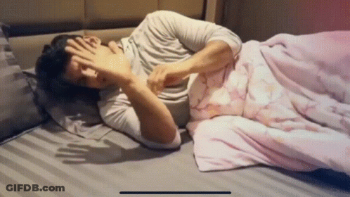 A Man Laying On A Bed With His Hand On His Face GIF