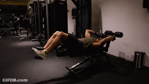 A Man Laying On A Bench In A Gym With A Machine That Says Technogym GIF
