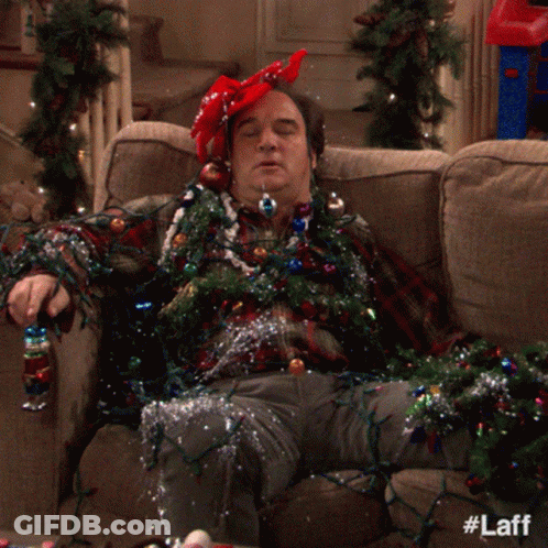 A Man Laying On A Couch Covered In Christmas Lights And Tinsel GIF