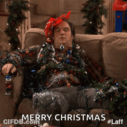A Man Laying On A Couch Covered In Christmas Lights With The Words Merry Christmas Below Him GIF