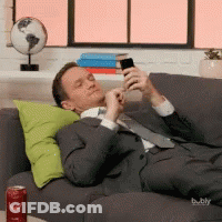 A Man Laying On A Couch Looking At His Phone GIF