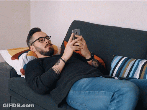 A Man Laying On A Couch Using A Cell Phone GIF