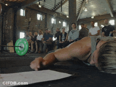 A Man Laying On The Floor With A Green Barbell That Says ' Rogue ' On It In Front Of A Crowd GIF
