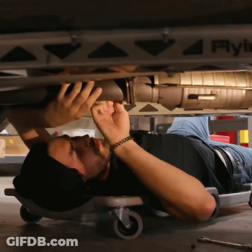 A Man Laying On The Floor Working Under A Car With A Sticker On The Side That Says Fly GIF