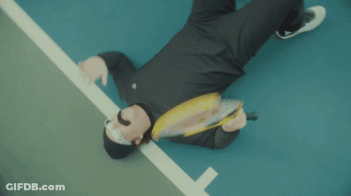 A Man Laying On The Ground Holding A Wilson Tennis Racquet GIF