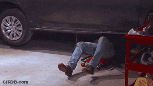 A Man Laying Under A Car In A Garage With A Sign That Says ' A ' On It GIF