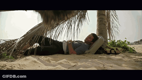 A Man Laying Under A Palm Tree On The Beach GIF