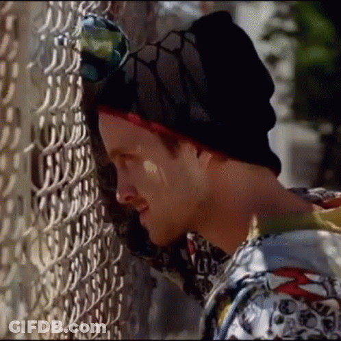 A Man Leaning Against A Chain Link Fence Wearing A Beanie And Sunglasses GIF