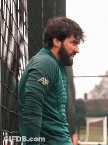 A Man Leaning Against A Fence Wearing A Green Sweater With Axa On The Sleeves GIF