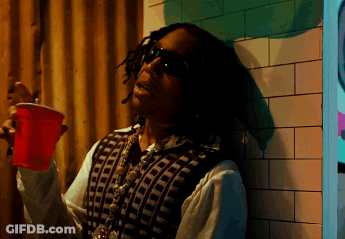 A Man Leaning Against A Wall Holding A Red Plastic Cup GIF