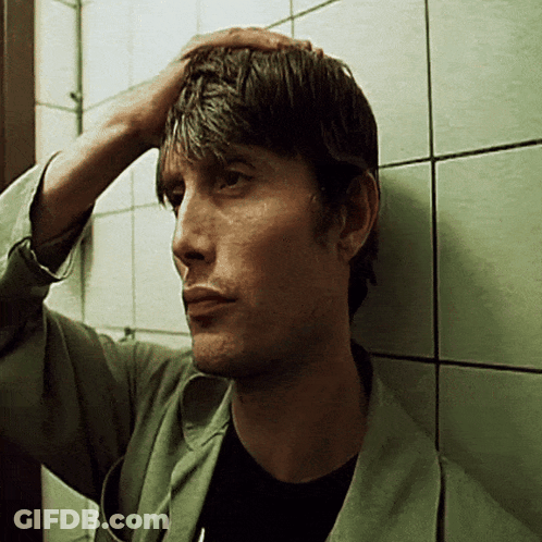 A Man Leaning Against A Wall Holds His Hand To His Head GIF