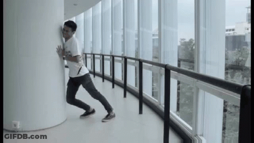 A Man Leaning Against A Wall In A Hallway With Lots Of Windows GIF