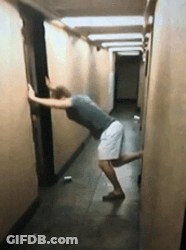 A Man Leaning Against A Wall In A Long Hallway GIF
