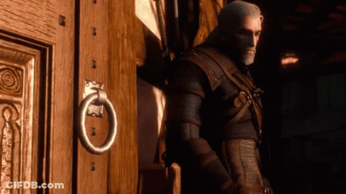 A Man Leans Against A Wooden Door With A Metal Ring On It GIF