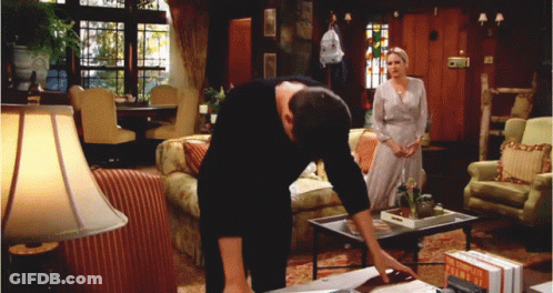 A Man Leans Over A Table In A Living Room With A Woman Standing In The Background GIF