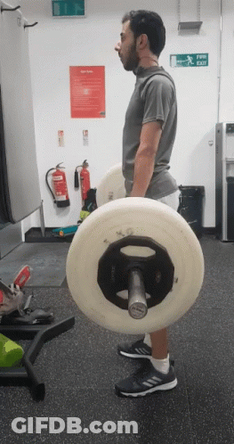 A Man Lifting A Barbell In A Gym With A Fire Extinguisher On The Wall Behind Him GIF
