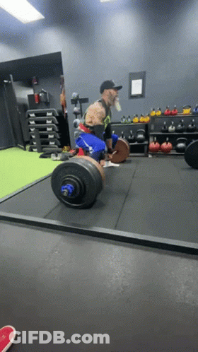 A Man Lifting A Barbell In A Gym With A Motorcycle In The Background GIF