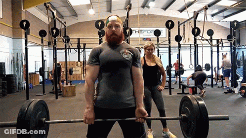 A Man Lifting A Barbell In A Gym With A Sign That Says The Fort GIF