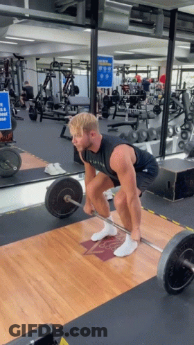 A Man Lifts A Barbell In A Gym While Wearing A Black Tank Top That Says ' Alpha ' On It GIF