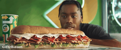 A Man Looking At A Subway Sandwich Next To A Cup That Says " Get " GIF