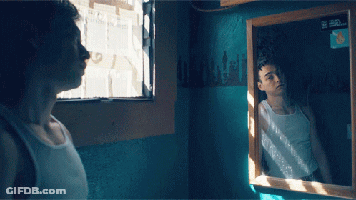 A Man Looking At His Reflection In A Mirror With A Sign On The Wall That Says ' A ' On It GIF