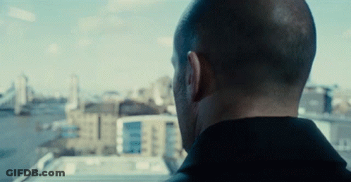 A Man Looking Out A Window With Buildings In The Background GIF