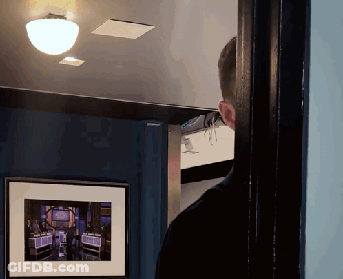 A Man Looking Through A Doorway At A Framed Picture Of A Game Show Called The Price Is Right GIF