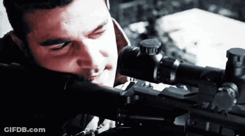 A Man Looking Through A Sniper Scope With A Red Light Behind Him GIF