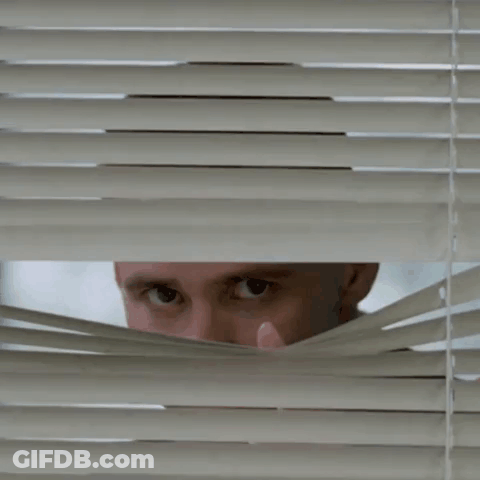 A Man Looking Through Blinds With His Hand On His Face GIF