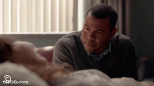 A Man Looks At A Woman Laying In A Hospital Bed With A C On The Bottom GIF