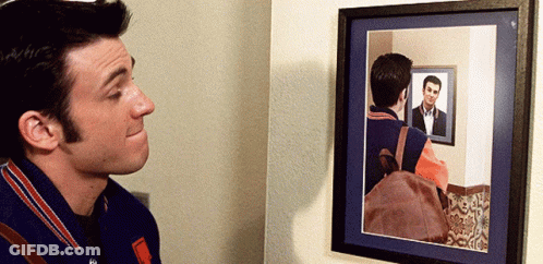 A Man Looks At His Reflection In A Mirror GIF