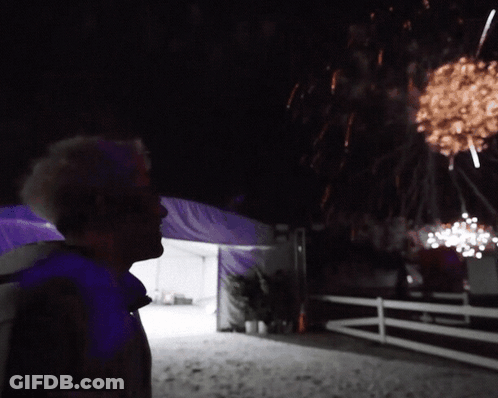 A Man Looks Up At A Fireworks Display In The Night Sky GIF