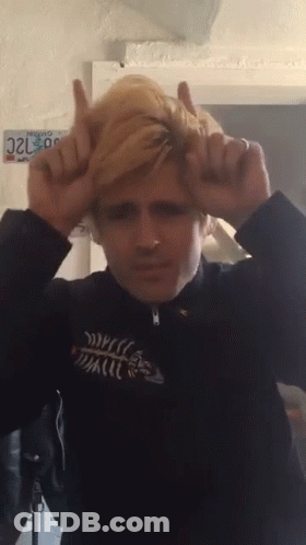 A Man Making A Devil Horns Gesture With A California License Plate Behind Him GIF