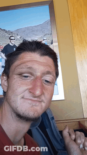 A Man Making A Funny Face In Front Of A Picture Of Two Men GIF