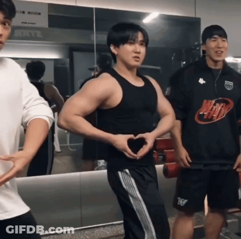 A Man Making A Heart Shape With His Hands In Front Of A Mirror In A Gym GIF